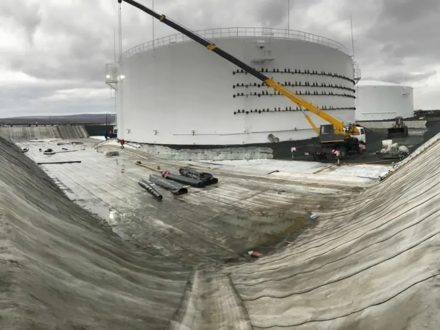 Long bund ridges around a storage tank under construction, covered continuously