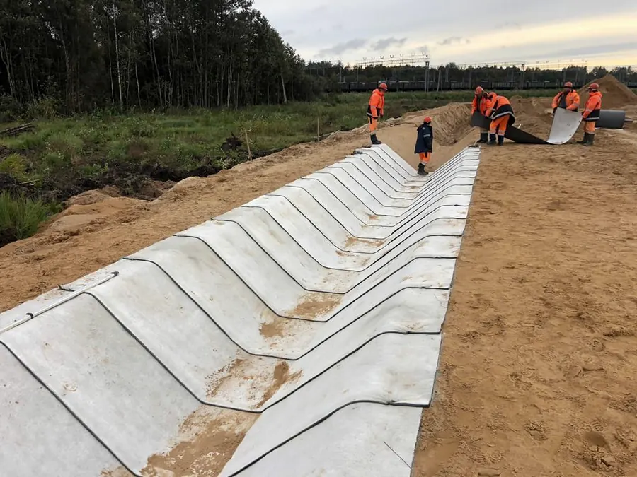 A drainage ditch with sheets laid transversely across the profile, workers continuing at the far end
