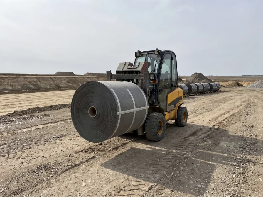 A rough-terrain forklift carrying a roll across an open construction site